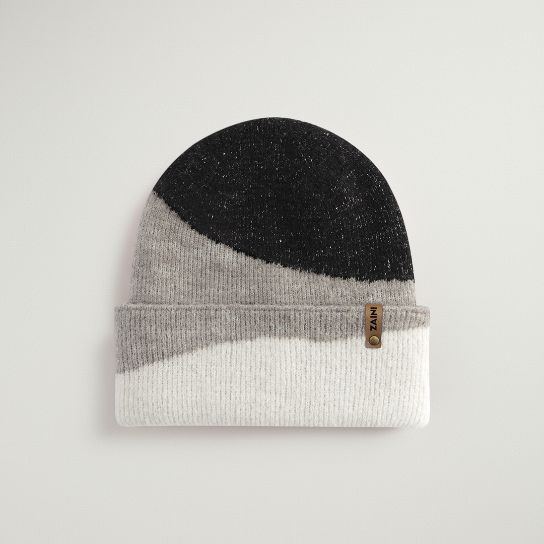 Color-blocked knit beanie with black, gray, and white sections on a light gray background