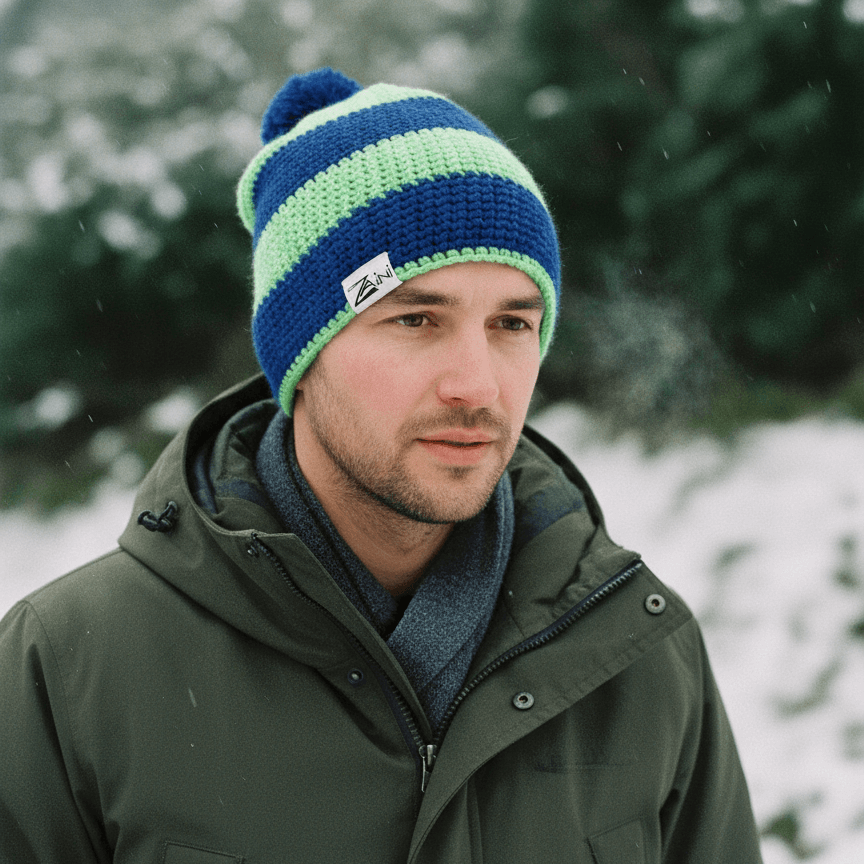 Man wearing a blue and green striped beanie with a logo, standing outdoors in a snowy landscape.