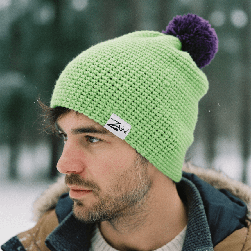 Man wearing a green knit beanie with a purple pom-pom in a snowy forest setting