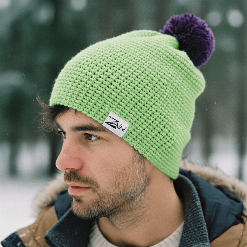 Man wearing a green knit beanie with a purple pom-pom in a snowy forest setting