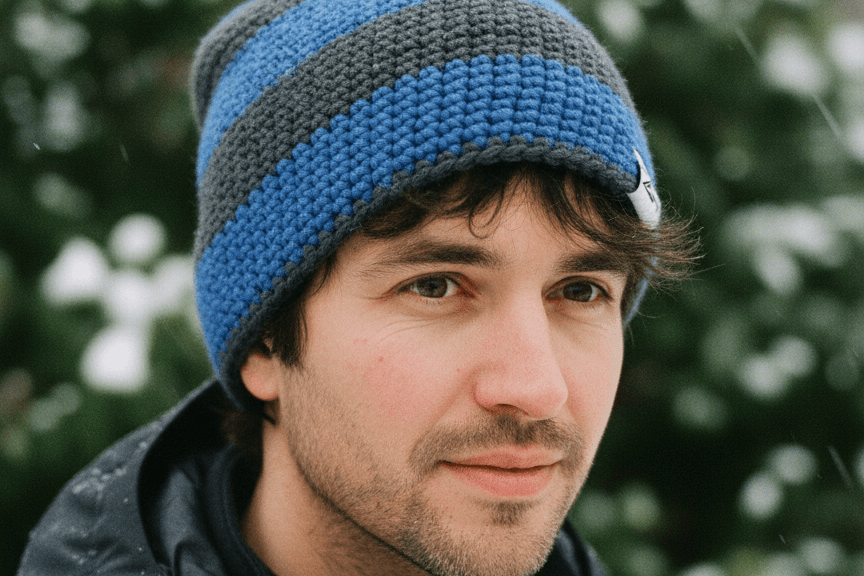 Man wearing a blue and gray striped knit beanie in a snowy outdoor setting