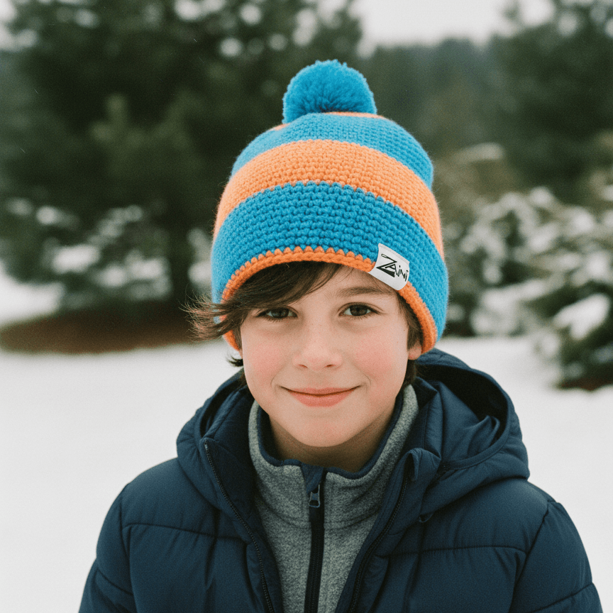 Child wearing a blue and orange striped knit hat in a snowy landscape with trees.