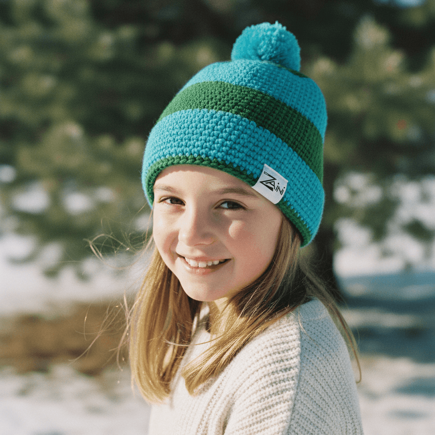Young girl wearing a green and blue striped knit beanie in a snowy outdoor setting.