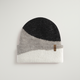 Color-blocked knit beanie with black, gray, and white sections on a light gray background