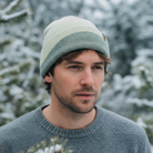 Man wearing a green beanie and sweater standing in a snowy forest