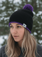 Woman wearing a black knit beanie with a purple pom-pom against a snowy background