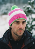 Man wearing a pink and white striped beanie with a green pom-pom in a snowy outdoor setting