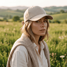 Woman wearing a beige cap and vest standing in a field with a scenic background