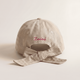 Beige cap with a bow and 'Zaini' branding on a light beige background