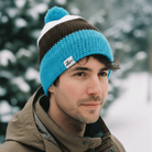 Man wearing a blue knit beanie with a pom-pom in a snowy forest setting