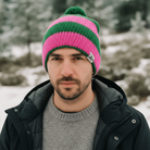 Man wearing a pink and green striped beanie in a snowy forest setting