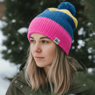 Person wearing a colorful knit beanie with a logo in a snowy outdoor setting