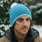 Man wearing a blue knit beanie with a white pom-pom in a snowy outdoor setting