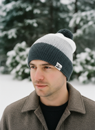 Man wearing a two-tone beanie with a logo in a snowy outdoor setting