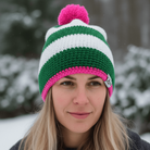 Person wearing a green and pink striped beanie with a pom-pom in a snowy outdoor setting