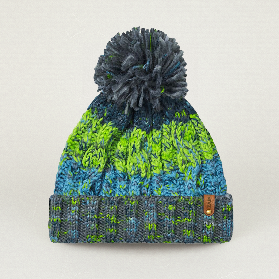 Knitted beanie with green and blue pattern and gray pom-pom on a light gray background