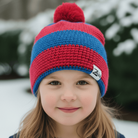 Child wearing a red and blue striped knit hat with a brand logo in a snowy background