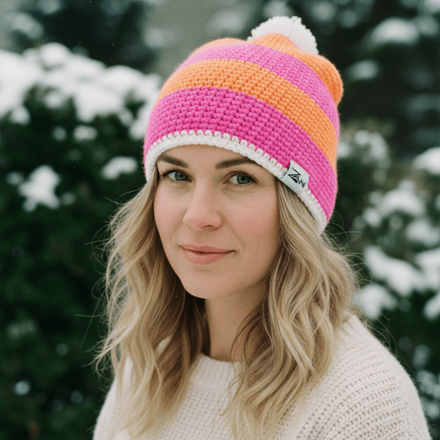 Woman wearing a colorful striped beanie with a brand logo against a snowy tree background