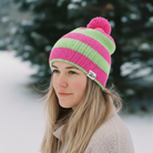 Person wearing a pink and green striped beanie with a pom-pom in a snowy outdoor setting.