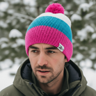 Person wearing a colorful knit beanie with a brand logo in a snowy outdoor setting