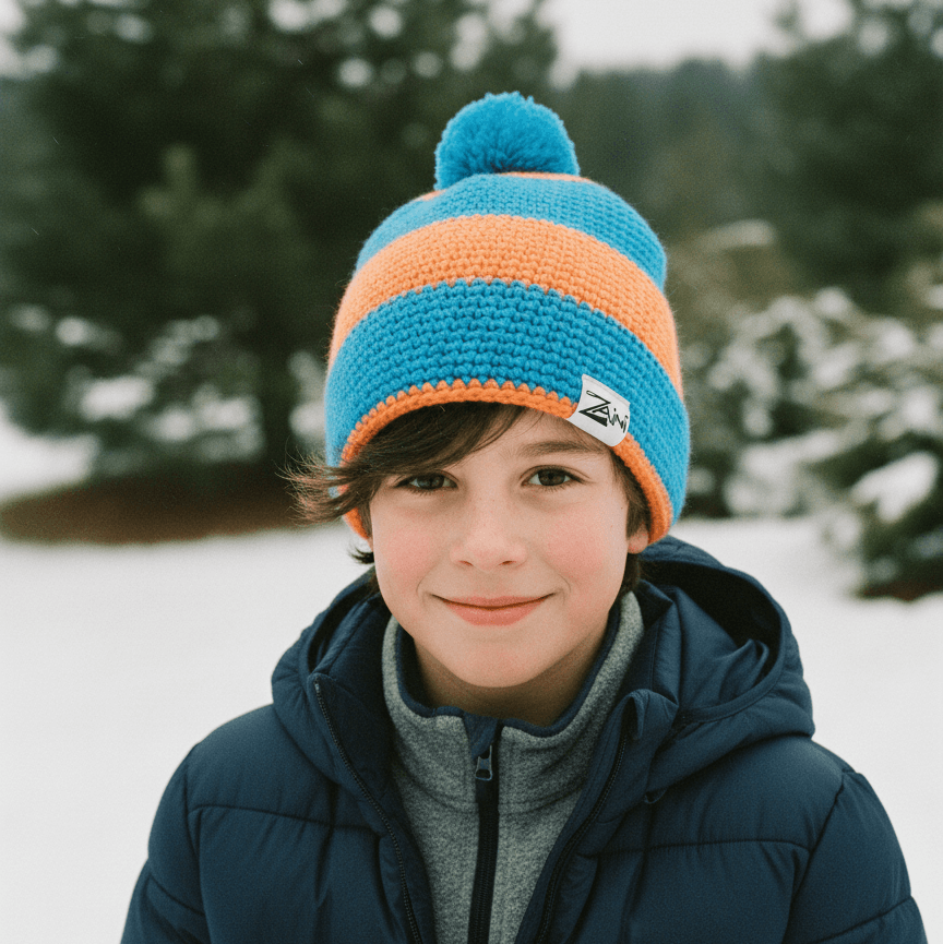 Child wearing a blue and orange striped knit hat in a snowy landscape with trees.