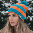 Person wearing a blue and orange striped beanie with a pom-pom in a snowy forest setting