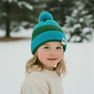 Child wearing a blue and green striped knit hat in a snowy landscape