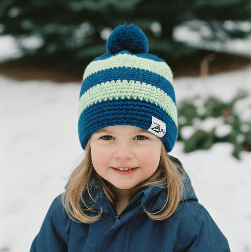 Child wearing a blue and green striped knit hat with a pom-pom in a snowy outdoor setting.