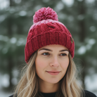 Woman wearing a red knit beanie with a pom-pom in a snowy forest setting