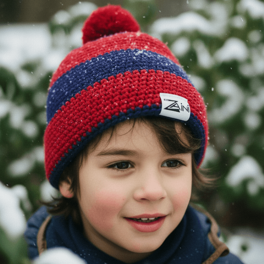 Child wearing a red and blue striped knit hat with a brand logo, standing in a snowy outdoor setting.