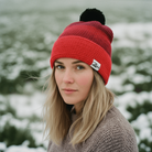 Person wearing a red knit beanie with a pom-pom in a snowy landscape