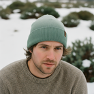 Man wearing a green beanie and brown sweater in a snowy landscape