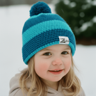 Child wearing a blue knit hat with a pom-pom in a snowy outdoor setting