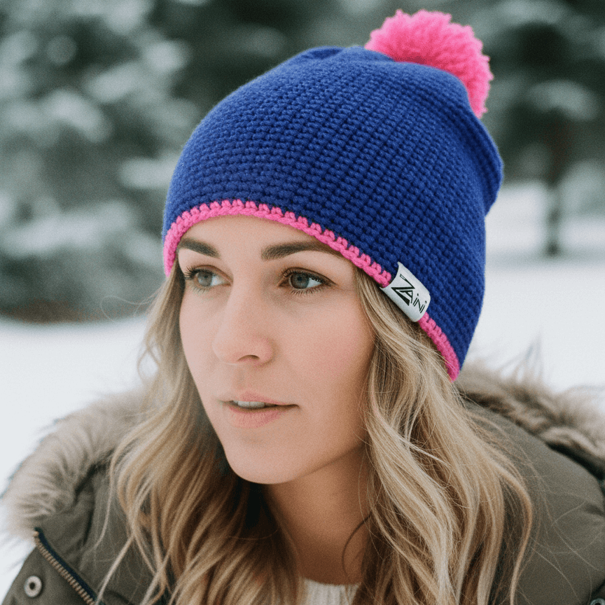 Person wearing a blue knit beanie with a pink pom-pom in a snowy landscape